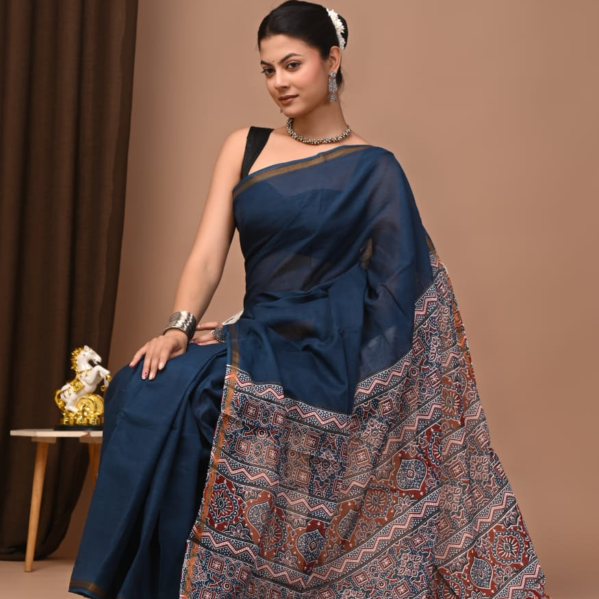 Woman in a blue saree with a patterned border against a brown background