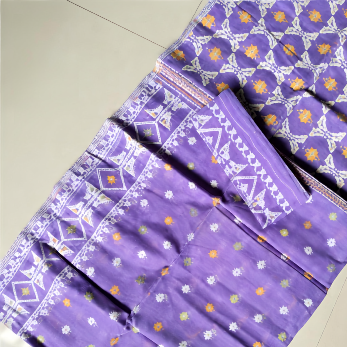 Purple cotton saree with white geometric border patterns and small multicolor floral prints, laid flat on a light beige tiled floor.