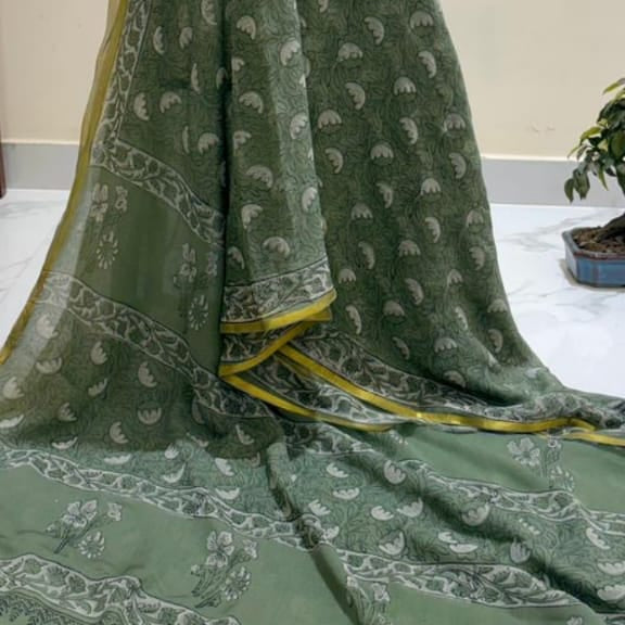 A sage green dupatta with white printed motifs and a yellow border, draped elegantly against a plain indoor wall.