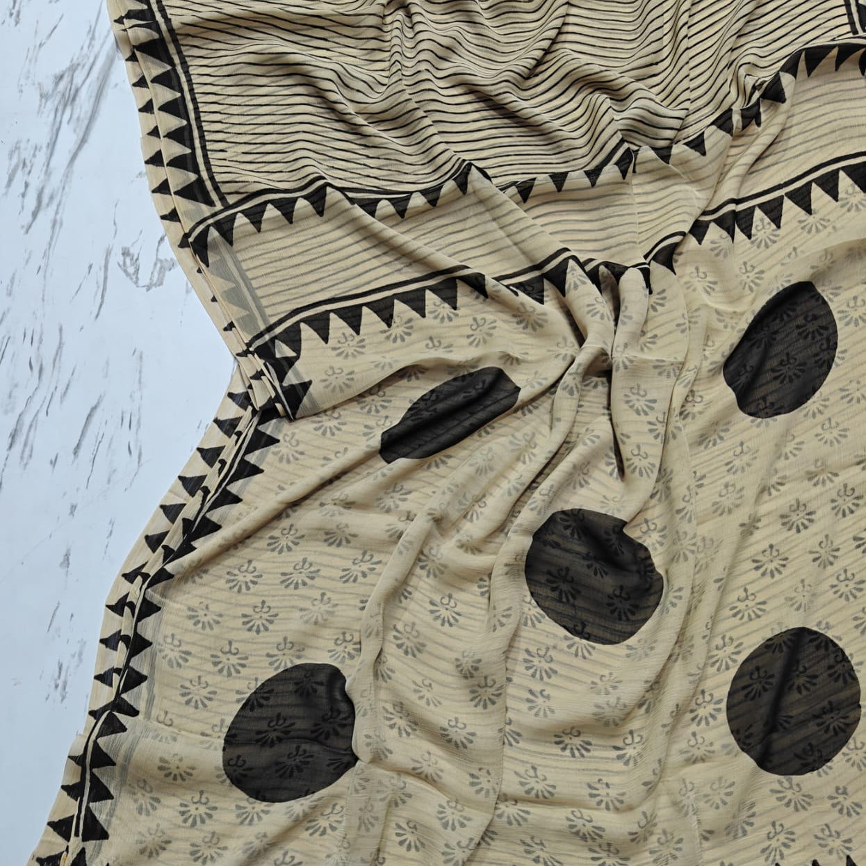 Beige and black patterned chiffon saree on a light blue background