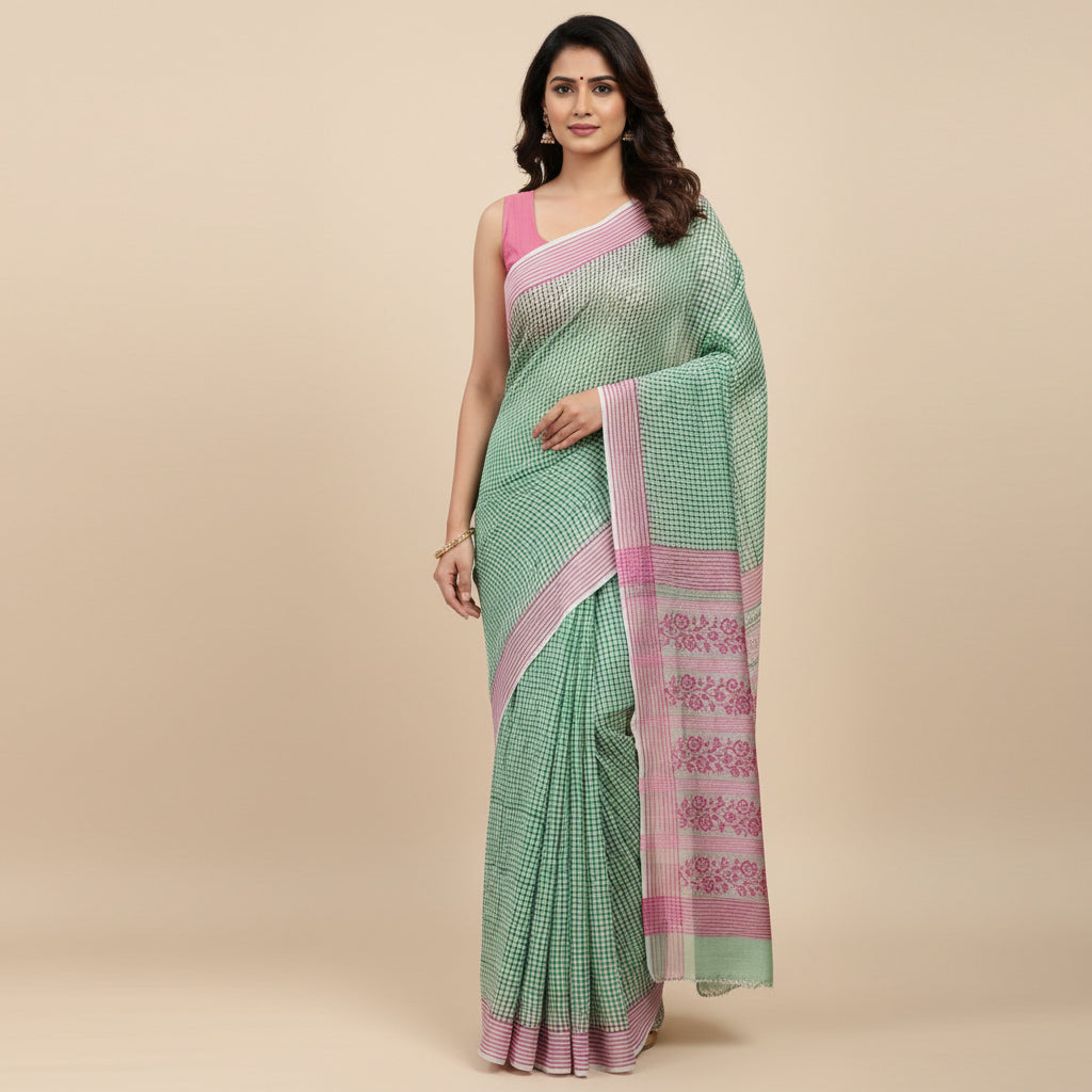 A green and pink checkered chiffon saree draped to show its pattern and border, laid flat on a light gray textured surface.