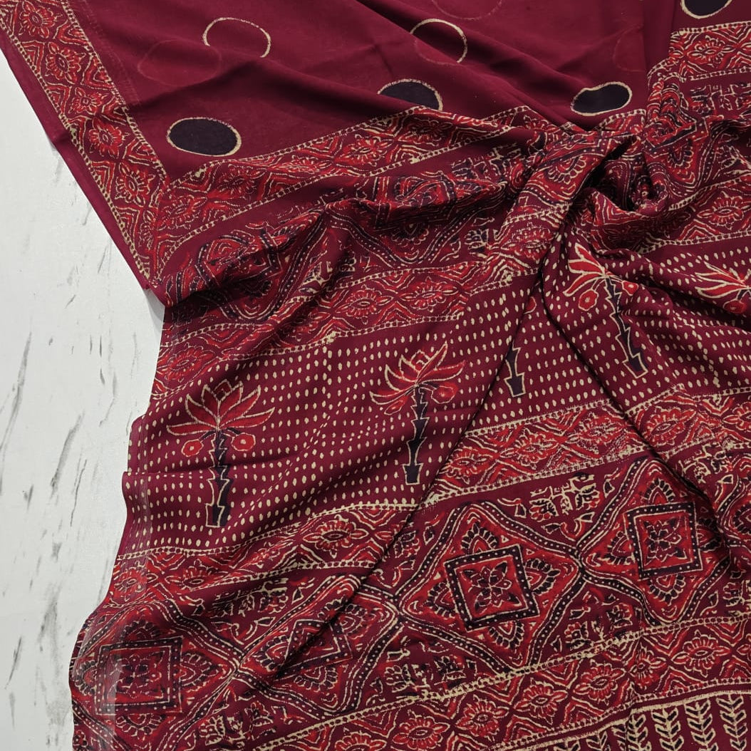 Maroon chiffon saree with intricate patterns on a light wooden surface