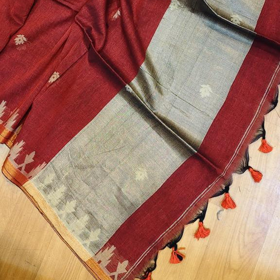 A deep red silk saree with small white floral motifs and a silver-gray border, laid out on a wooden floor.