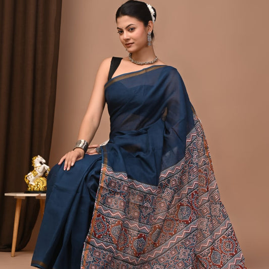 Woman in a blue saree with a patterned border against a brown background